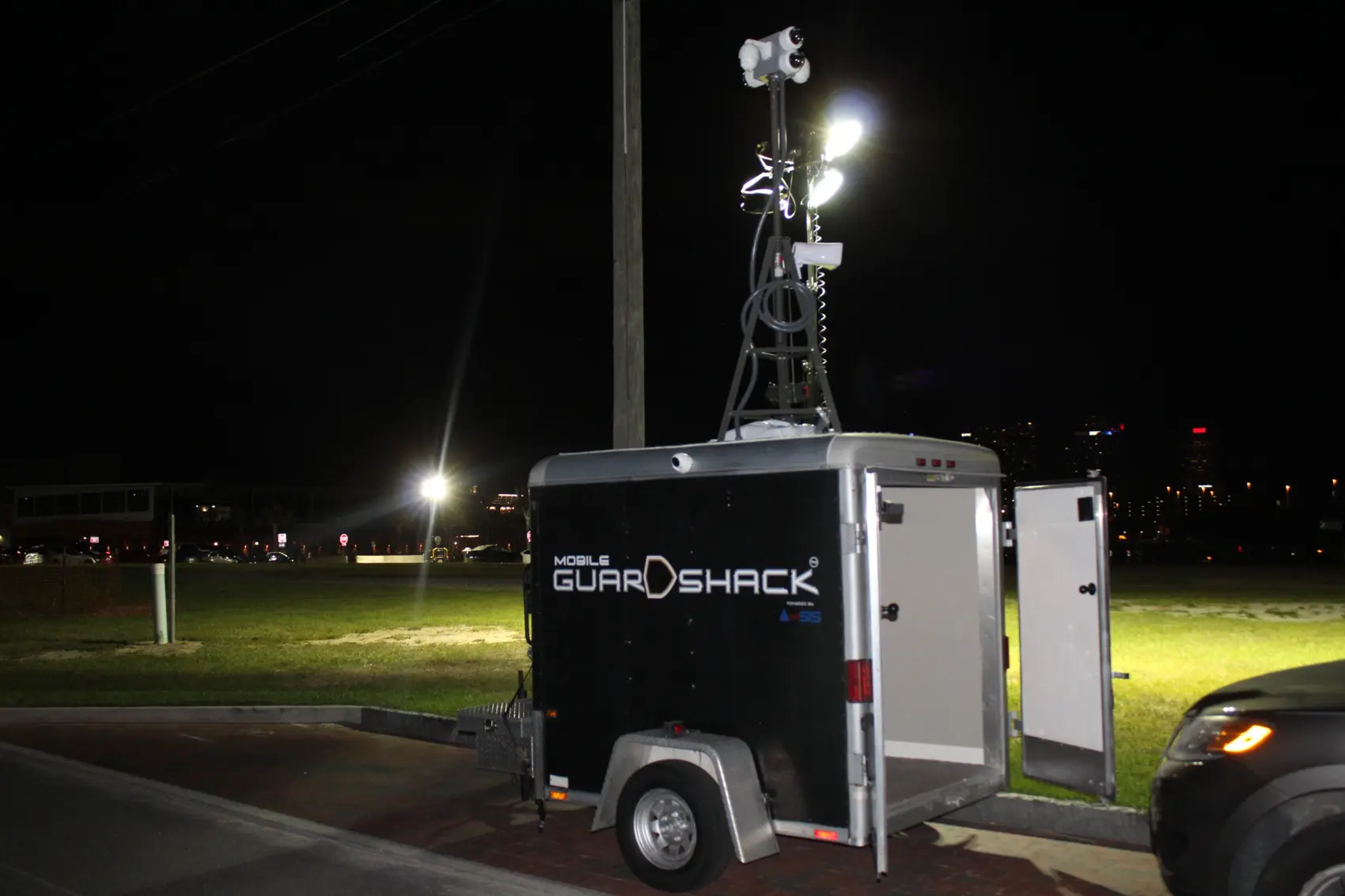 Mobile GuardShack with rear doors open, exterior work lights and extended surveillance mast at night